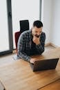 Young man with beard working on laptop at desk in a modern office setting.